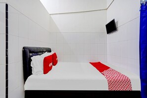 A hotel room with a bed, white tiled walls, a mounted TV, and a blue curtain.