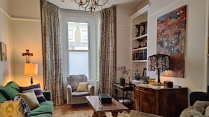 A living room with a green sofa, a beige armchair, a wooden coffee table, and a bookshelf. - Elegant Victorian house in South London. Excellent transport links. (London)