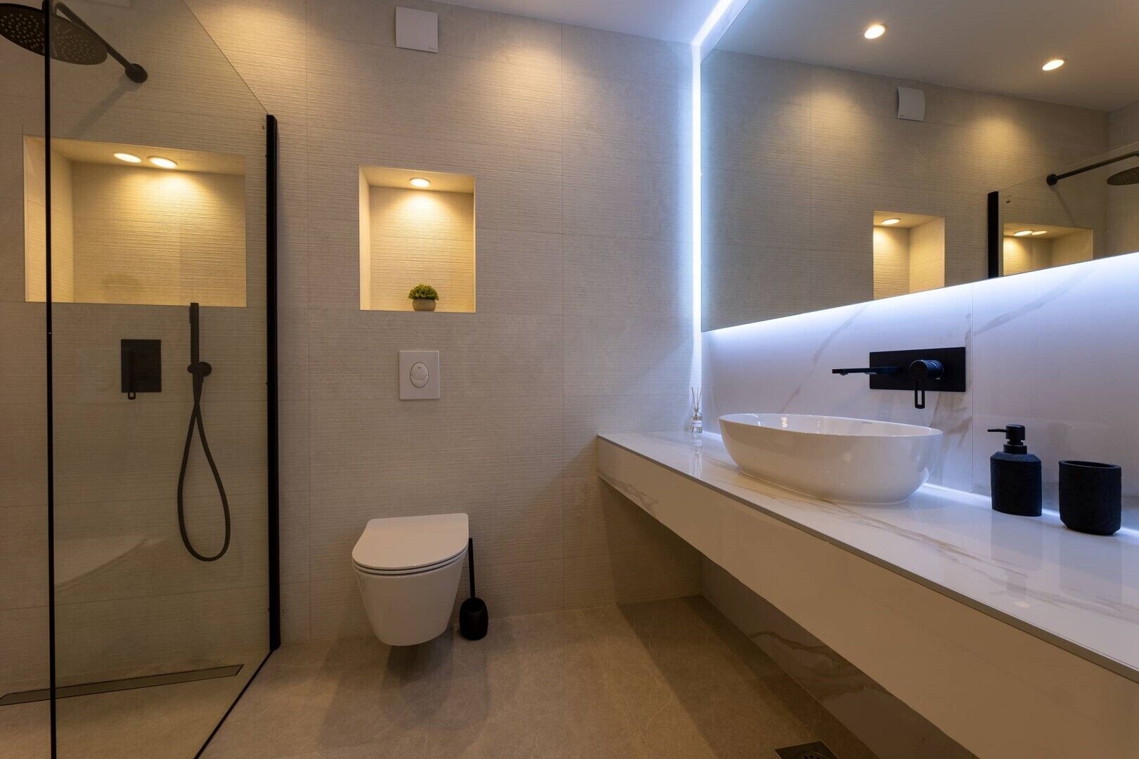 A modern bathroom with a glass-enclosed shower, a white toilet, a large vessel sink, and a mirror above the sink.