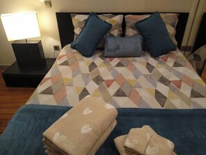 A neatly made bed with a patterned bedspread, two pillows, and a folded blanket on a wooden floor.