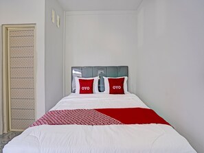 Habitación de hotel con una cama, dos almohadas con la marca 'OYO', un plaid rojo y blanco y un cabecero gris.