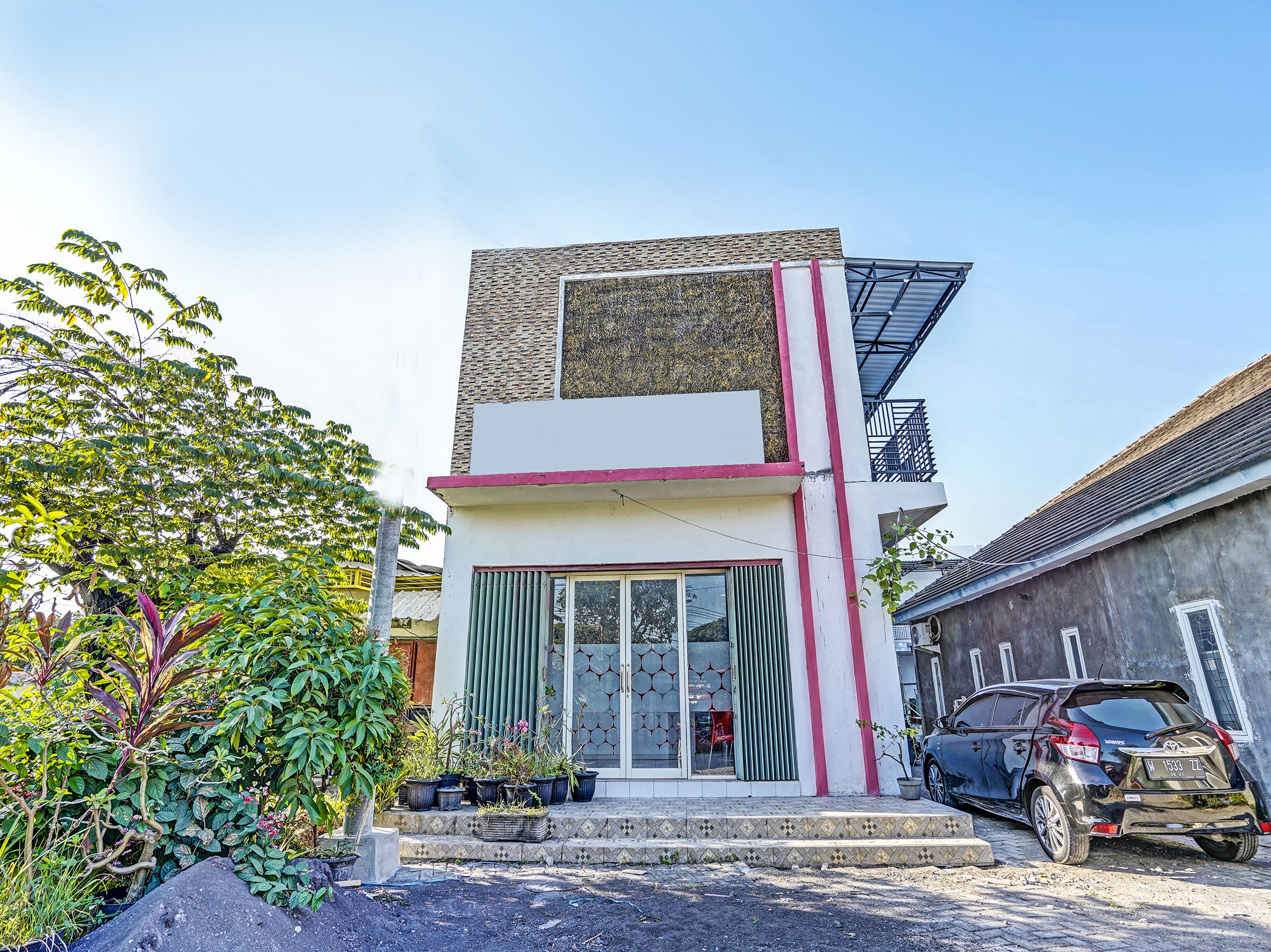 Et moderne hus med to etager, fladt tag og en balkon, med en bil parkeret foran.