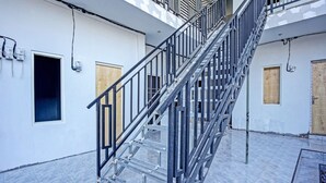 A metal staircase with a handrail leading to a landing. There are two doors on the landing, one with a window, and a wall-mounted electrical box. - OYO LIFE 91594 Bungah Residence Syariah (Gresik)