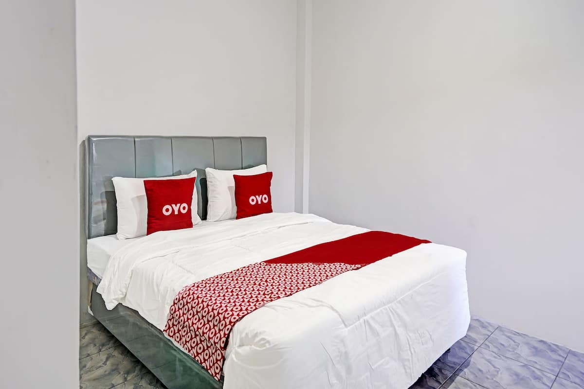 A neatly made bed with white and red bedding, a grey headboard, and a red and white patterned throw.