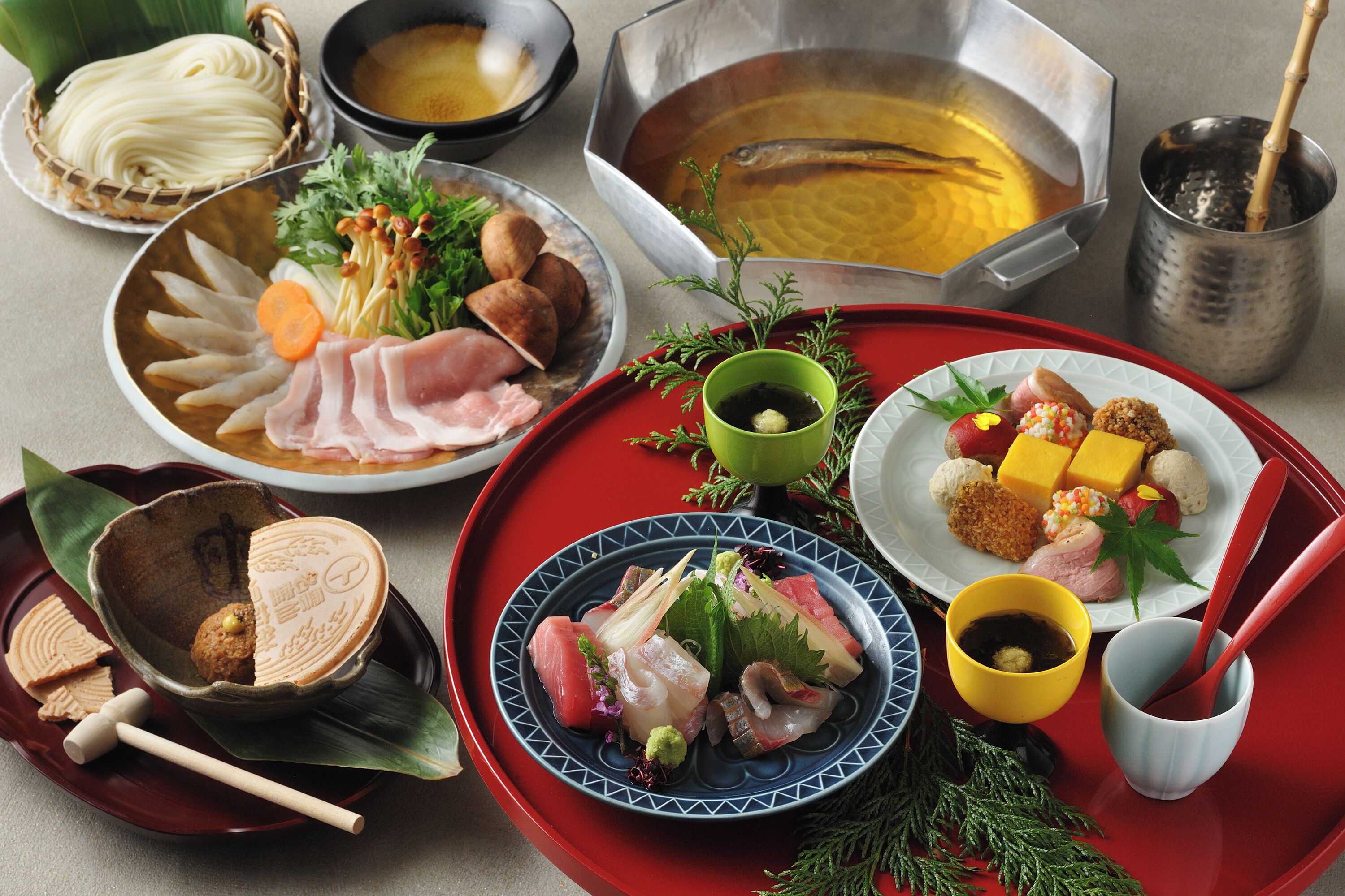 Variedade de pratos japoneses, incluindo sashimi, macarrão e um cozido, dispostos em uma bandeja.