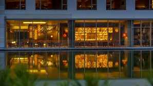 A modern hotel with a large glass facade, a pool in the foreground, and a well-lit interior with seating areas. - Hoshino Resorts KAI Unzen (Unzen)