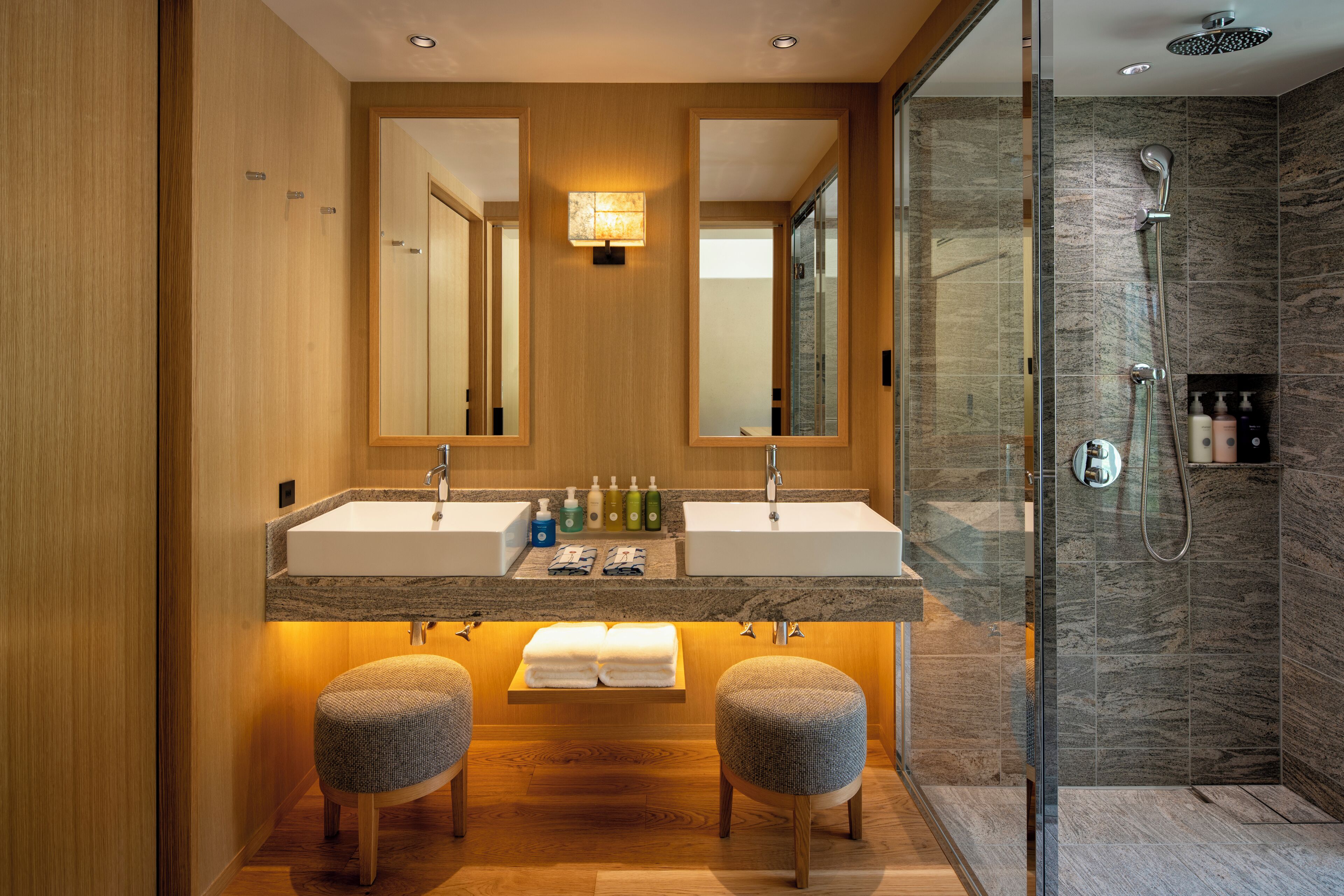 A modern bathroom with a wooden vanity, dual sinks, and a glass-enclosed shower area.
