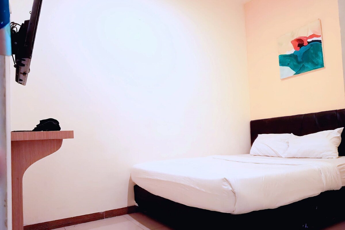 A single bed with white bedding in a room with a wooden headboard and a small wooden shelf.
