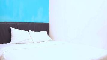 Una cama bien hecha con ropa blanca y un cabecero oscuro en una habitación con una pared azul decorativa y un cuadro.
