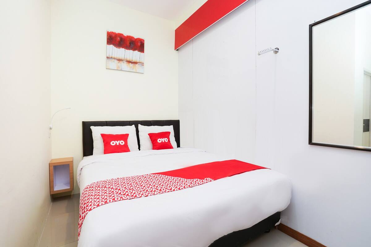 A neatly made bed with a white and red patterned bedspread, two red pillows, and a red accent wall.
