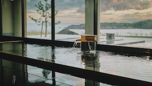 A modern indoor pool with a view of a coastal landscape, including trees and mountains. - Hoshino Resorts KAI Izumo (Izumo)