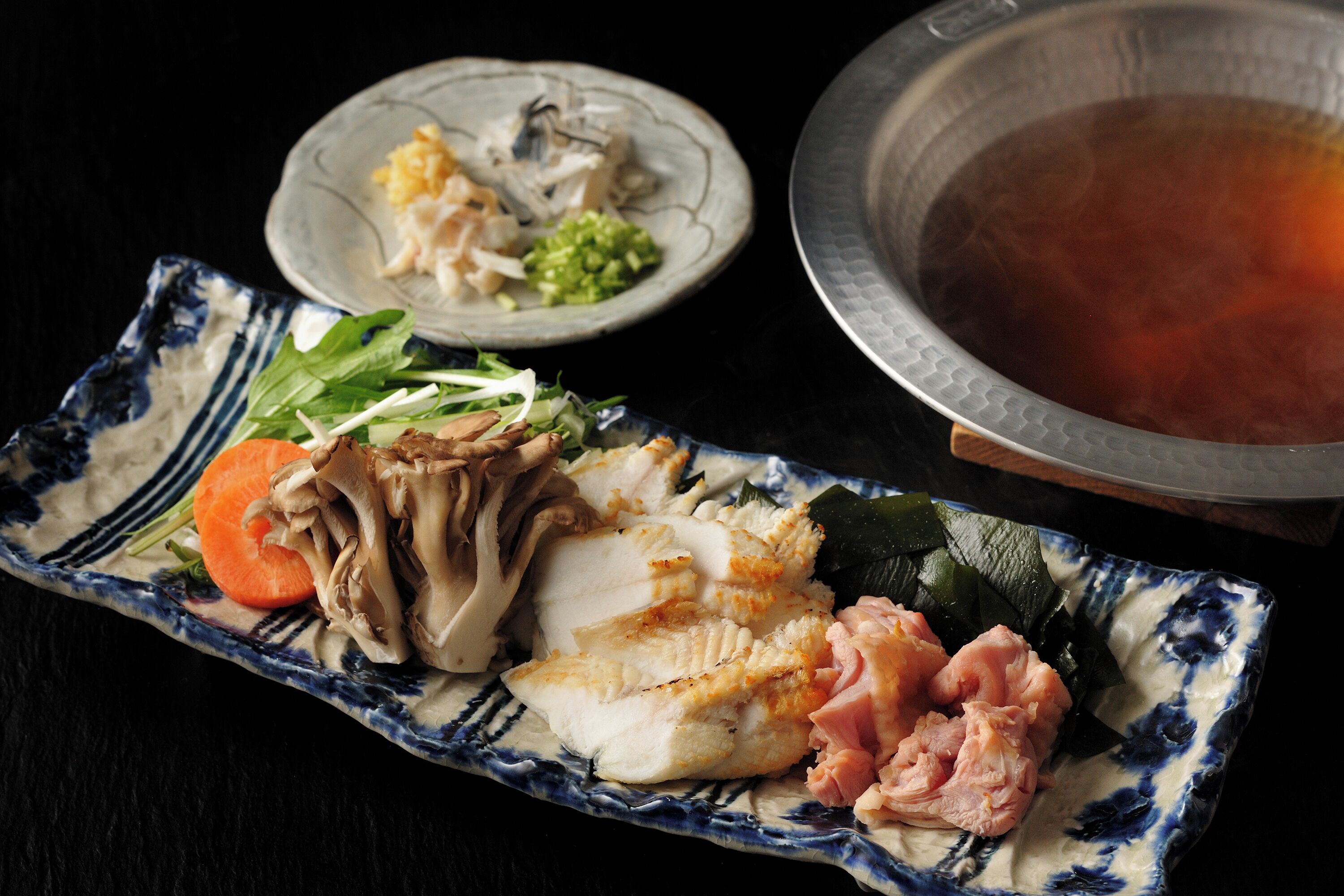 A traditional Japanese meal with various dishes on a blue and white ceramic plate, including fish, vegetables, and a bowl of soup.