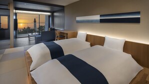 A modern hotel room with two beds, a desk, and a view of a sunset through large windows. - Hoshino Resorts KAI Izumo (Izumo)