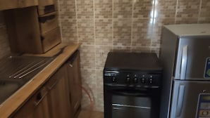 Una cocina con armarios de madera, un lavamanos de acero inoxidable, una estufa negra y un refrigerador.
