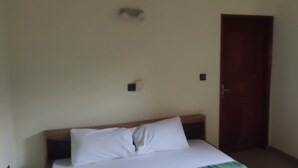 Una habitación con una cama, cabecera de madera, una puerta y un interruptor de luz en la pared.