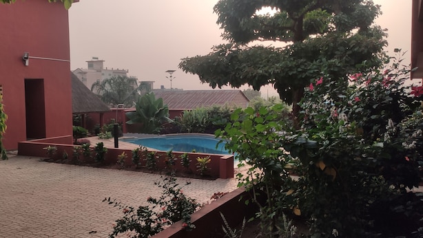 Un patio con piscina, rodeado de plantas en macetas y un edificio rojo.