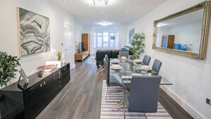 A modern dining area with a glass table, dark wood flooring, and a large mirror on the wall. - Newly Refurbished Modern 4 Bed Detached House (oxford)