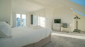 A bedroom with a large bed, a desk with a chair, a television, and a coat rack. - Newly Refurbished Modern 4 Bed Detached House (oxford)