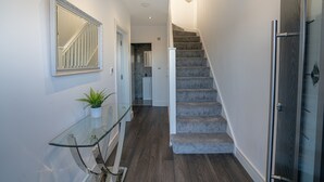 A modern hallway with a glass console table, a potted plant, a staircase with carpeted steps, and a door with a glass panel. - Newly Refurbished Modern 4 Bed Detached House (oxford)