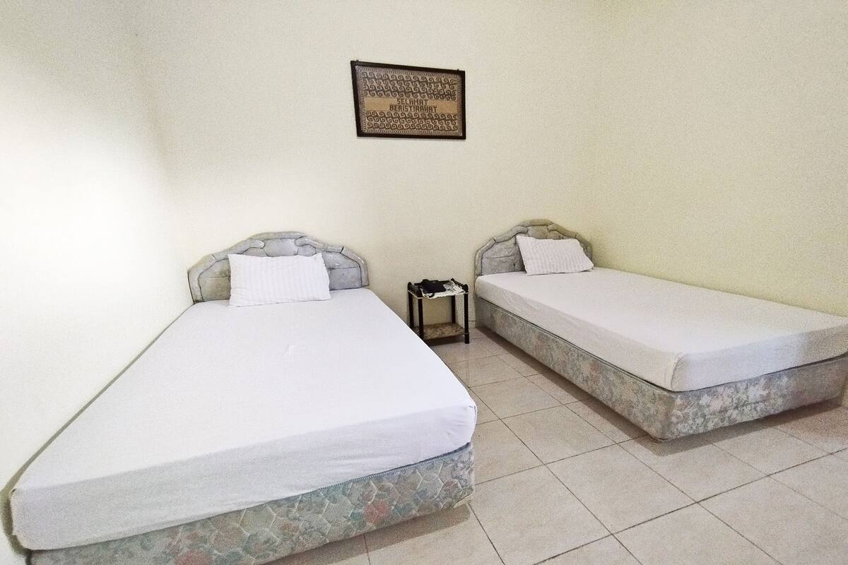 Deux lits simples avec des têtes de lit en pierre, dans une chambre dont le sol est recouvert de carreaux.