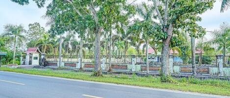 A road lined with trees and a gated area with a small building.