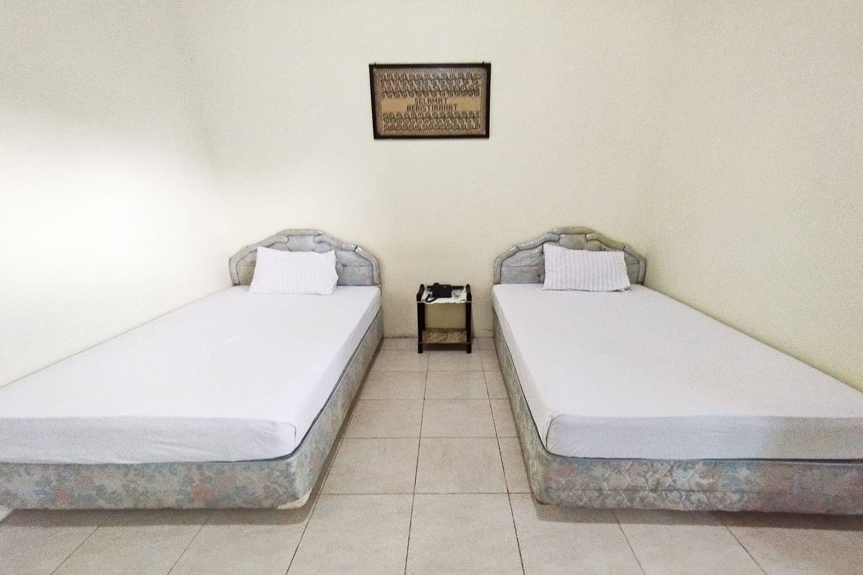 A room with two single beds, a small bedside table with a lamp, and a framed picture on the wall.