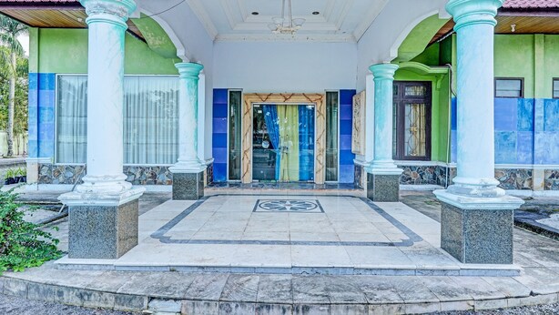 Un bâtiment doté d’une façade verdoyante, de touches de couleur bleue et d’une entrée centrale avec un sol carrelé et un motif en forme d’étoile.