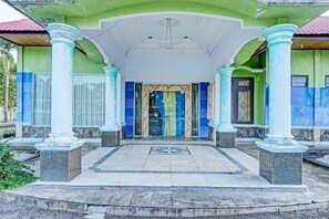 Un bâtiment doté d’une façade verdoyante, de touches de couleur bleue et d’une entrée centrale avec un sol carrelé et un motif en forme d’étoile.