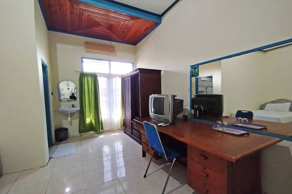 Une pièce comprenant un bureau en bois, une télévision, un lit, une fenêtre avec des rideaux et un petit lavabo.