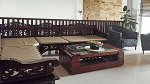Un canapé traditionnel en bois, doté d’assises rembourrées, et une table basse en verre agrémentée d’un arrangement floral.
