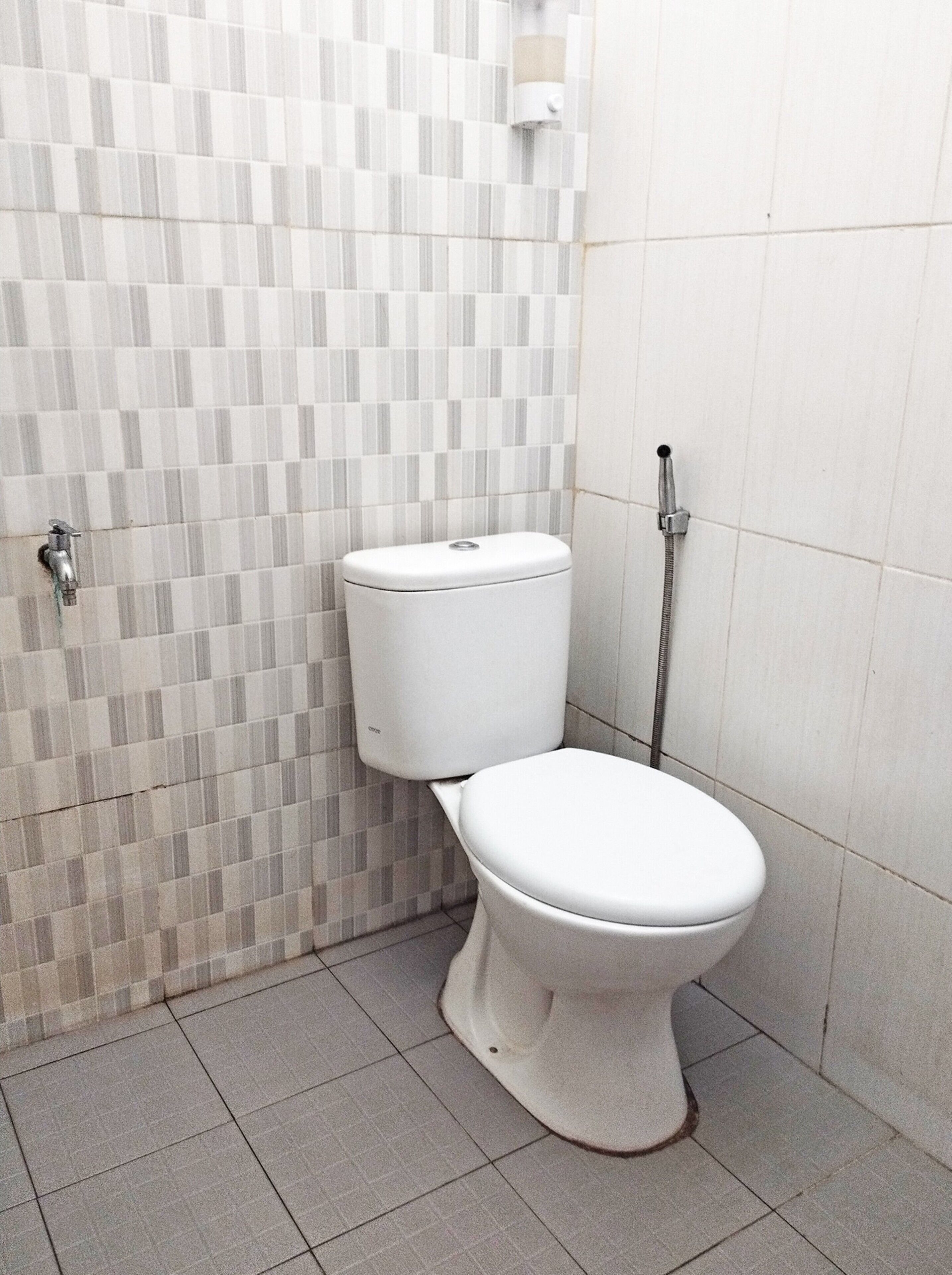 Un bagno piccolo rivestito di piastrelle, con il water, una doccia e un dispenser di sapone a parete.