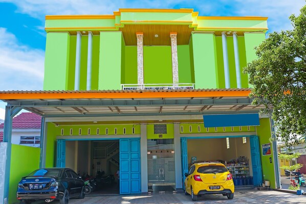 A brightly colored building with two open garages, a yellow car parked inside, and a black car parked outside. - Hotel O Homestay Anitha Syariah Makassar (Makassar)