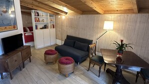 Un salon chaleureux avec un plafond en bois, un canapé, un téléviseur, une bibliothèque et une table à manger avec des chaises.