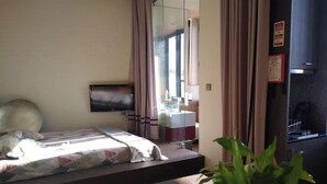 Een hotelkamer met een bed, een televisie, een kleine tafel en een plant in pot.
