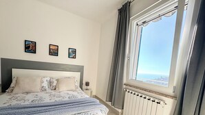 A bedroom with a large bed, a window with a view, and three pictures on the wall.
