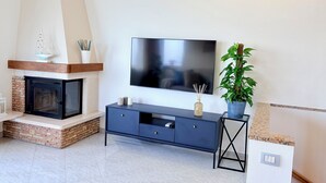 A modern living room with a fireplace, a TV mounted on the wall, a dark blue entertainment unit, and a potted plant.