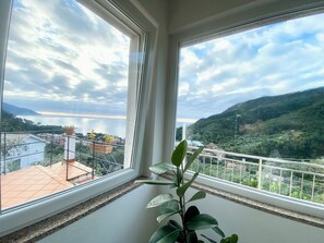 Uma varanda com vista para um lago e colinas, plantas em vasos e um corrimão.