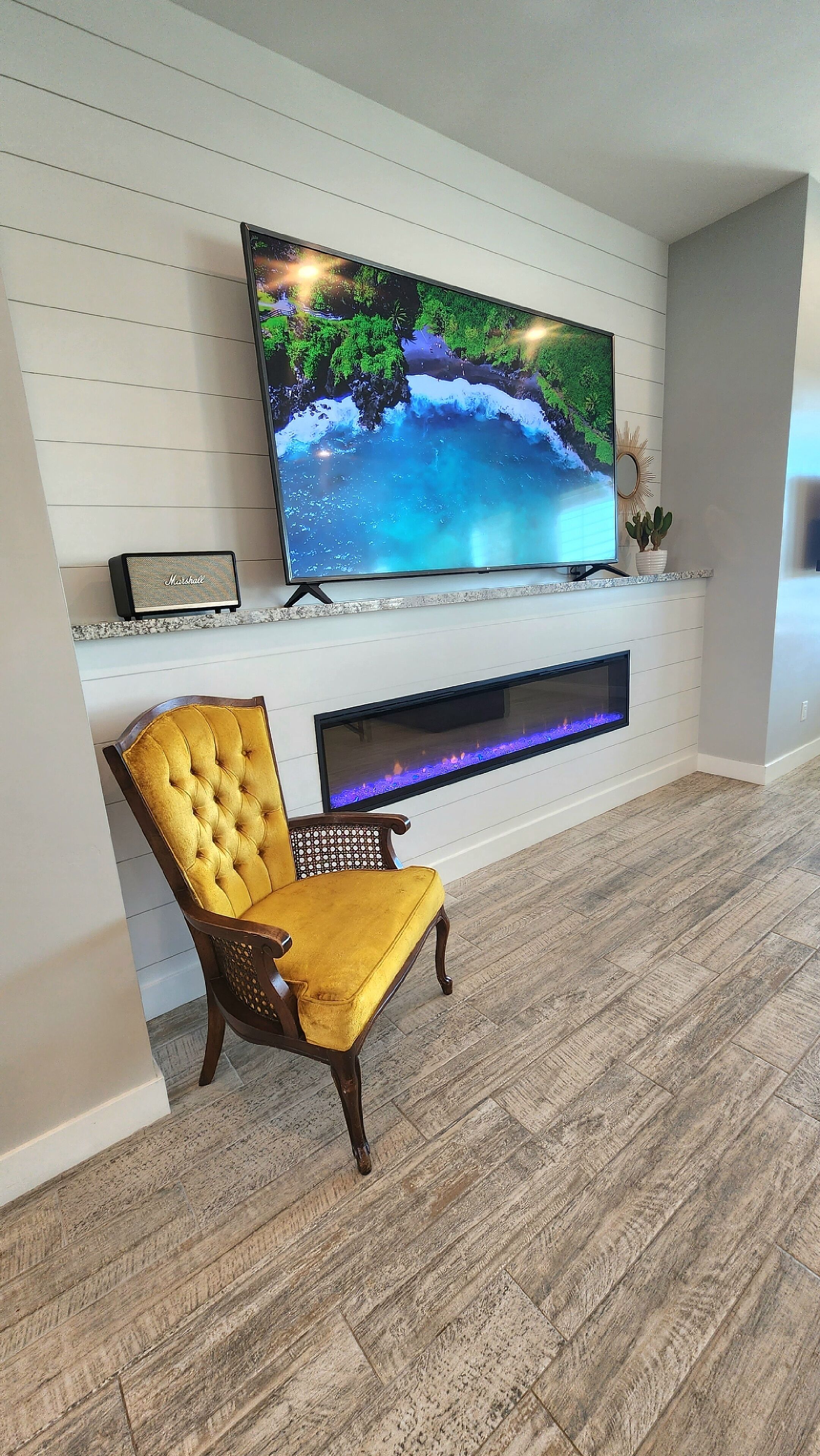 A modern living room with a flat-screen TV mounted on a white wall, a fireplace below, and a yellow upholstered armchair.