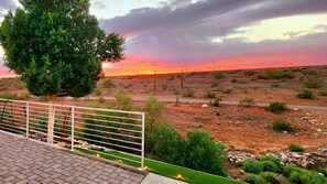 Paisagem desértica com pôr do sol, uma árvore e uma cerca.