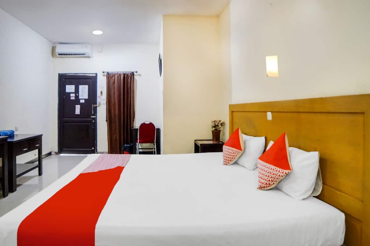 A hotel room with a large bed, a wooden headboard, a desk, and a chair.