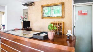 A reception desk with a television, a plant, and a framed Quran on the wall. - OYO 91878 Cherry Red Hotel (Medan)