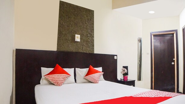A hotel room with a large bed, a dark headboard, and a red and white bedspread. - OYO 91878 Cherry Red Hotel (Medan)