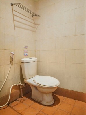 A standard white toilet with a wall-mounted hand dryer and a visible pipe, likely for flushing. - OYO 91878 Cherry Red Hotel (Medan)