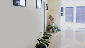 A hallway with a series of potted plants, framed pictures on the wall, and a door with a number. - OYO 91878 Cherry Red Hotel (Medan)