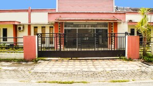 A building with a gated entrance, a tiled pavement, and a palm tree. - OYO 91878 Cherry Red Hotel (Medan)