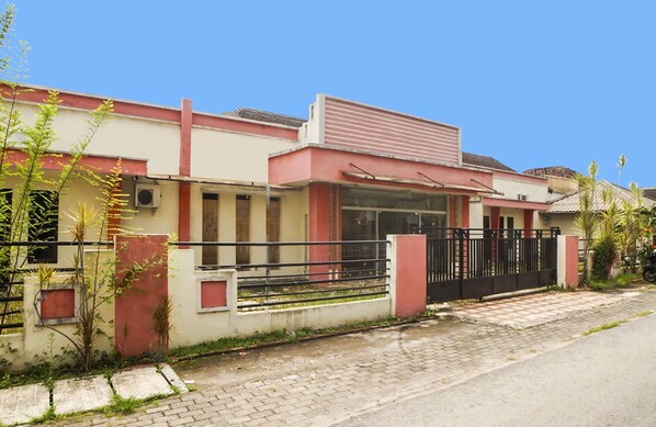Una casa de dos pisos con fachada roja y blanca, un acceso con portón y un camino de entrada pavimentado.