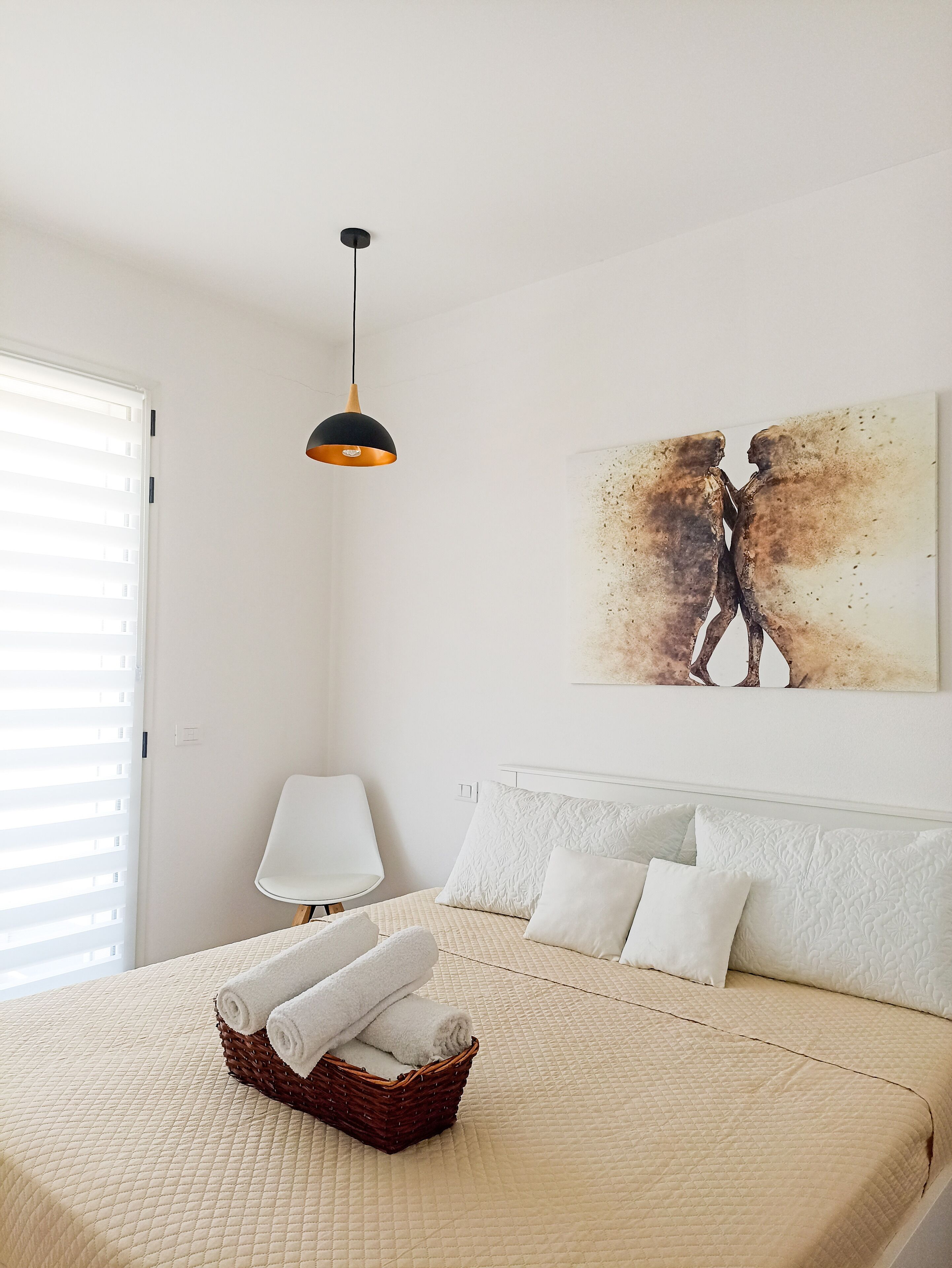 Ein Schlafzimmer mit Bett, einer Wandlampe, einem Gemälde und einem Fenster mit Jalousien.