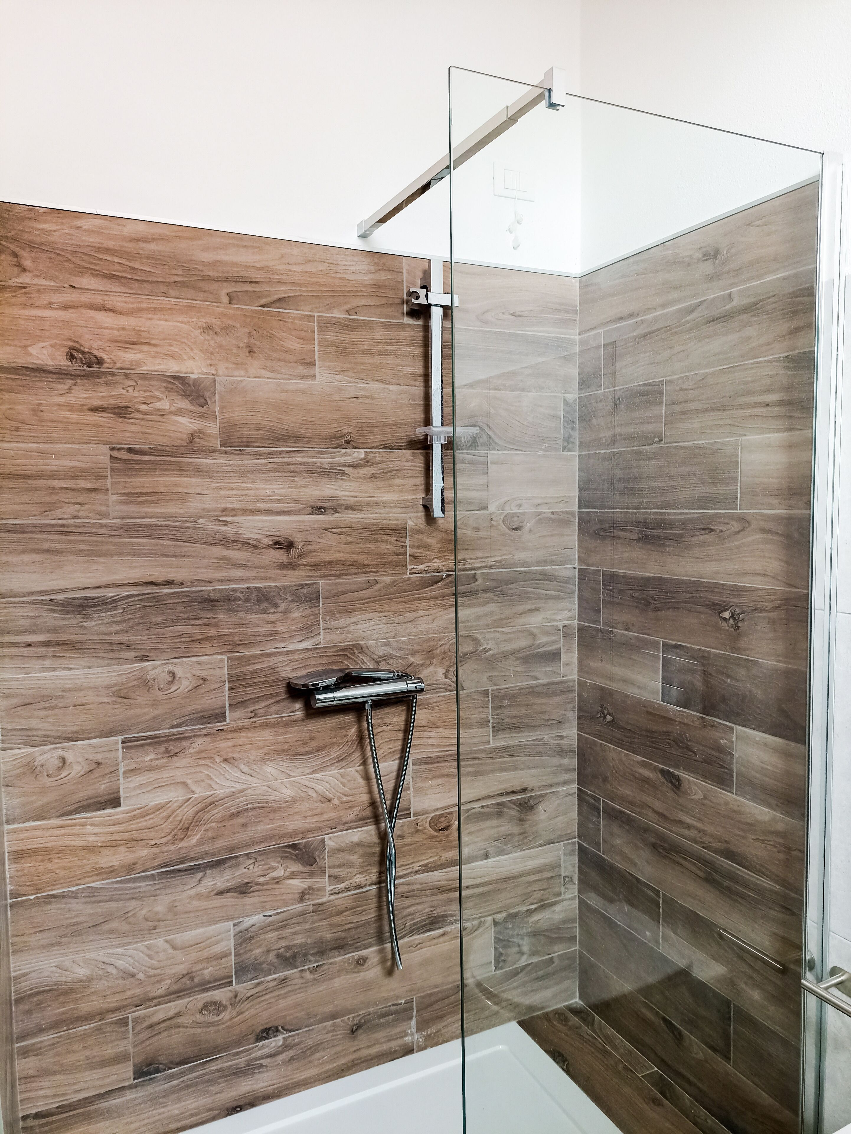 A shower area with a glass door, wooden wall tiles, and a handheld showerhead.