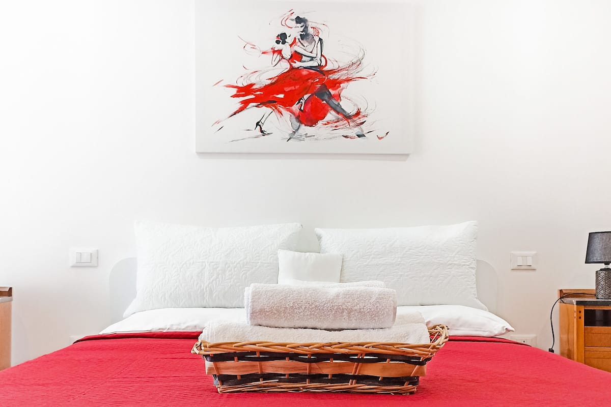 A neatly made bed with a red quilt, white pillows, and a woven basket on the bed.