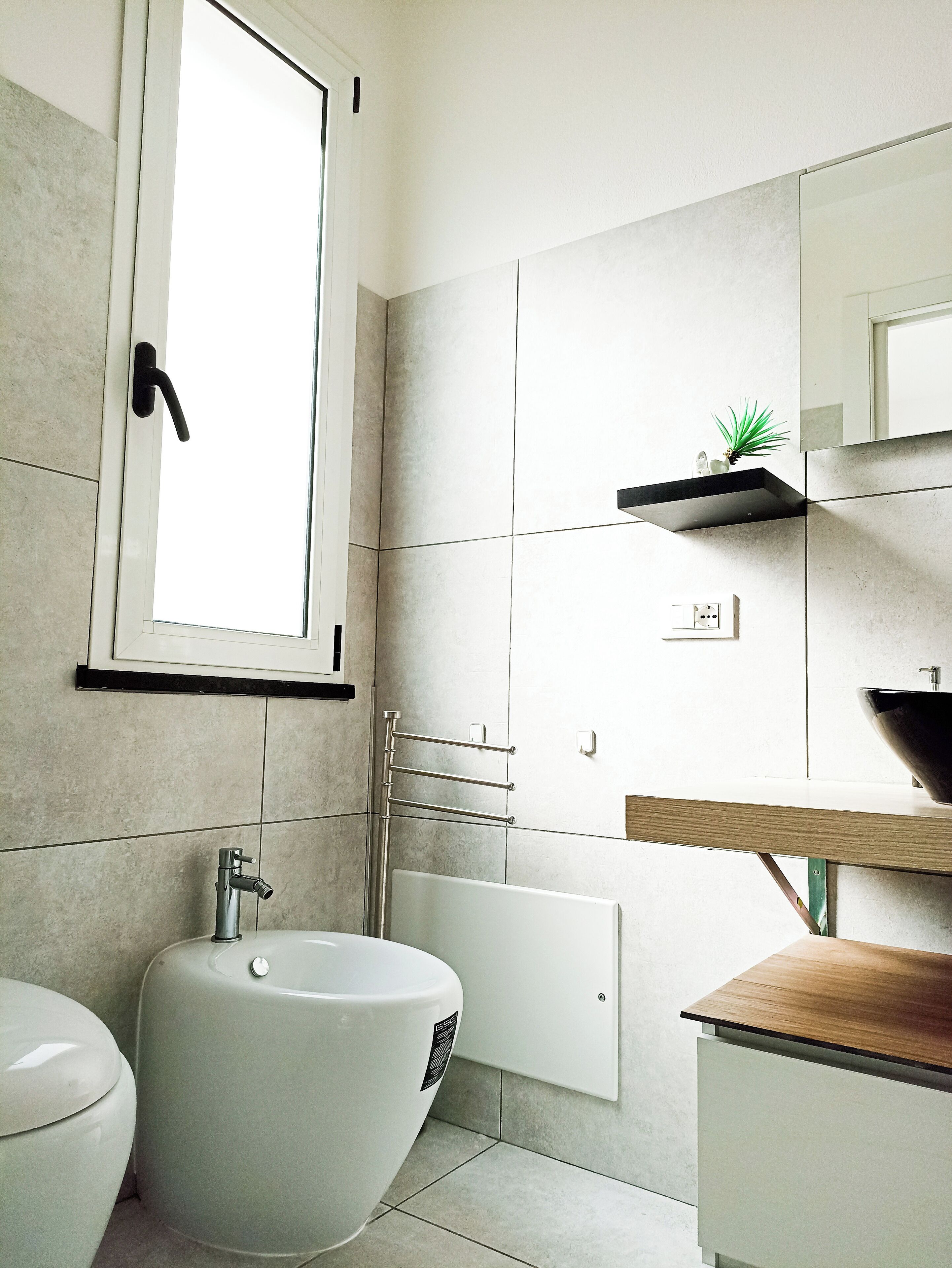 Et moderne badeværelse med toilet, bidet og en vask med træbordplade.